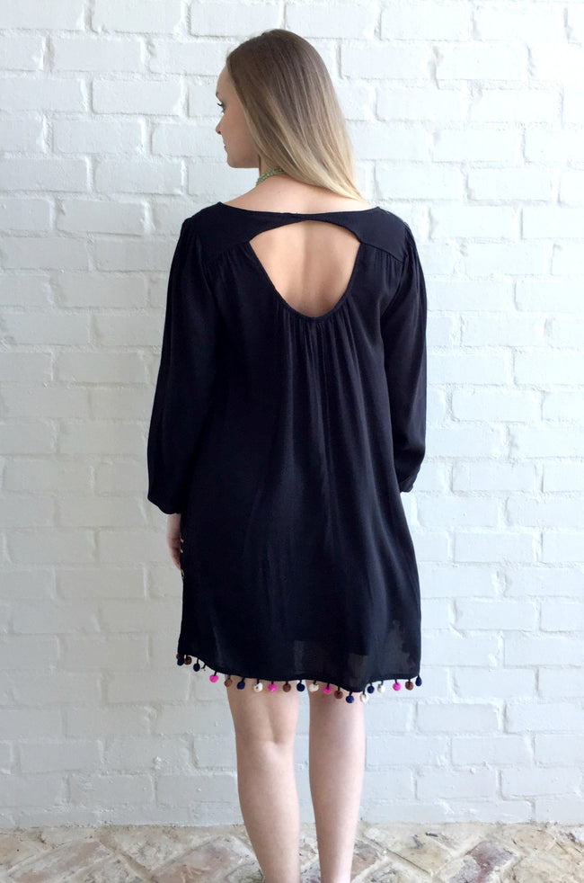 This tunic dress by Jodifll is perfect for vacation or a night out!The solid V-neck tunic dress has a colorful embroidered detail, a pom pom hem, and long tie sleeves. 